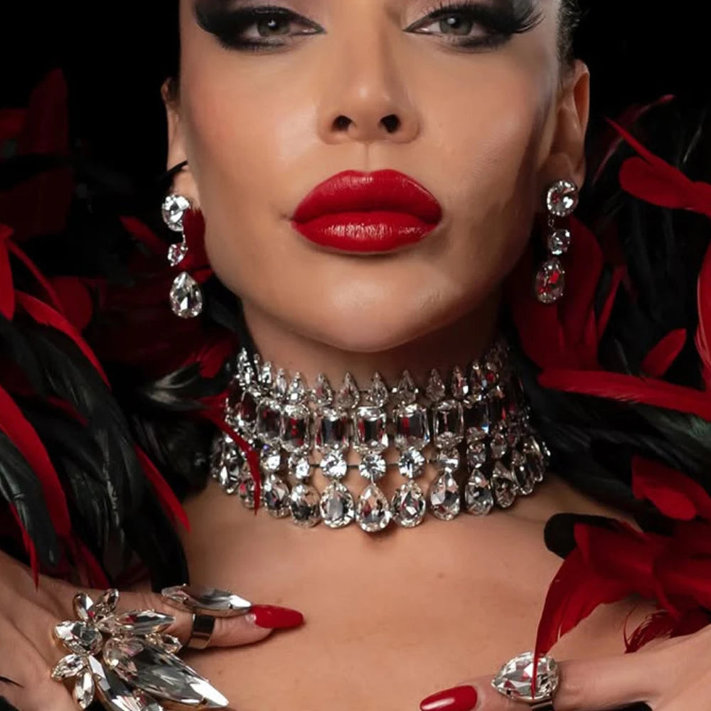 Close-up of a person wearing a sparkling necklace with red flowers and jewelry in the background